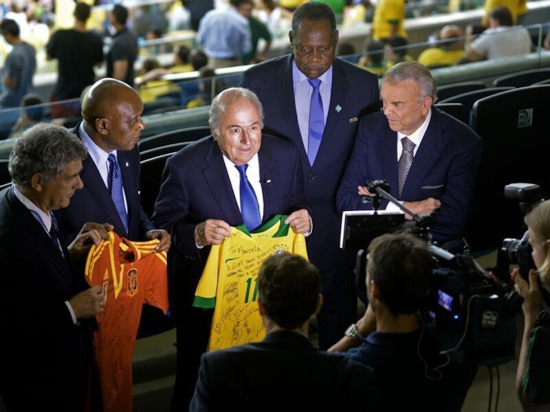 Voetbalofficials, met in het midden FIFA-voorzitter Blatter, houden de gesigneerde shirts omhoog.