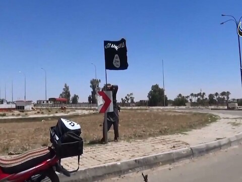 Een IS-strijder plant een vlag van de terreurbeweging in een straat van Ramadi.