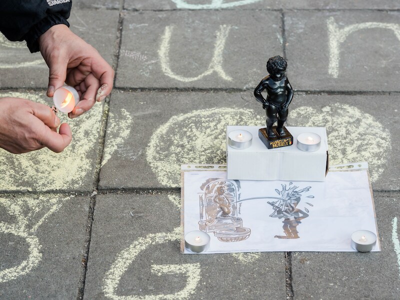 Een man ontsteekt een kaars naast een beeldje van Manneken Pis op het Beursplein in Brussel, de dag van de aanslagen.