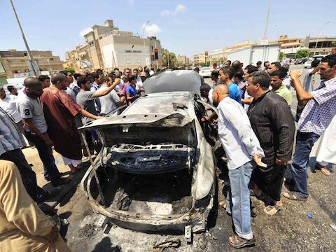 Omstanders bekijken het wrak van een auto na ontploffing van een autobom in Benghazi, dinsdag.