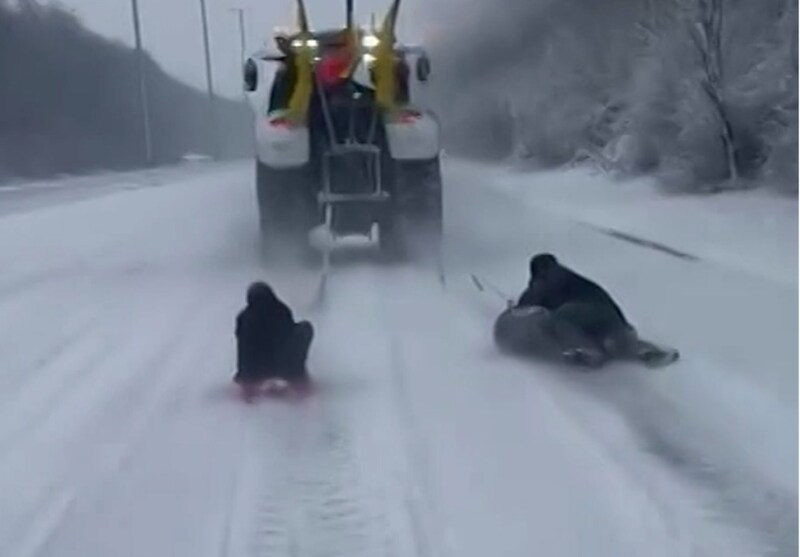 Los agricultores se mueven en trineo y son arrastrados por un tractor en la desierta E411