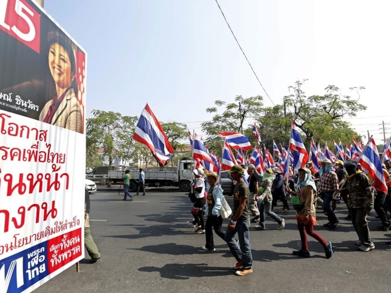 Demonstranten in Bangkok lopen langs een poster van de zittende premier Yingluck Shiwanatra.