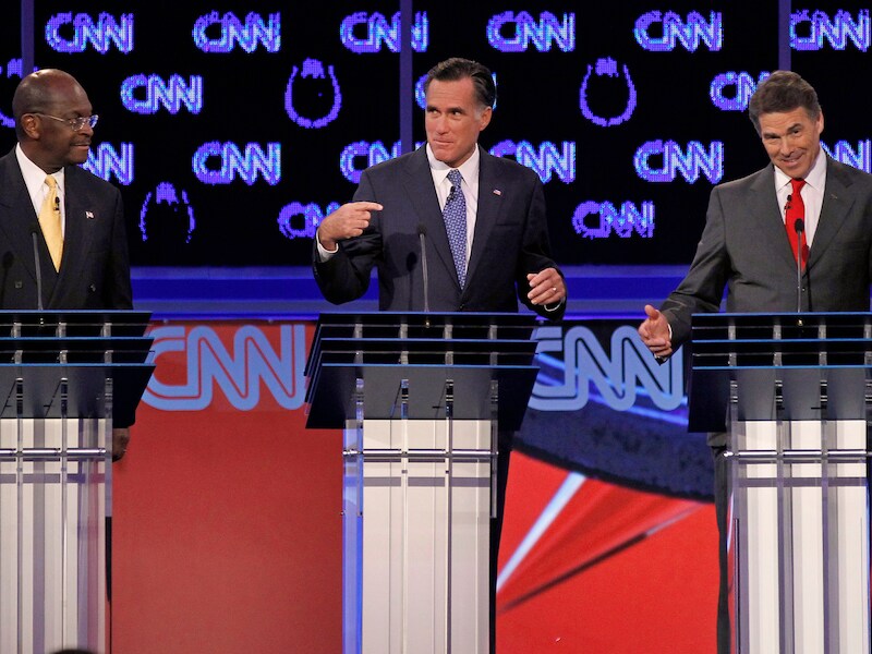 Herman Cain (L) beschuldigt Rick Perry (R), die de zwarte piet dan weer doorschuift naar Mitt Romney (C).