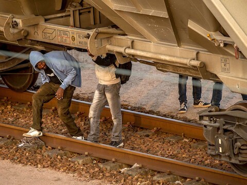 Migranten verbergen zich onder een goederentrein die via de Eurotunnel naar Engeland gaat.