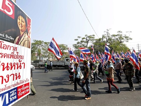 Demonstranten in Bangkok lopen langs een poster van de zittende premier Yingluck Shiwanatra.