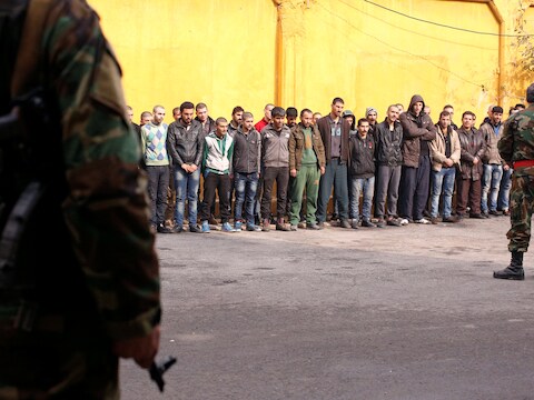 De militaire politie bewaakt mannen die uit de oostelijke wijken van Aleppo werden geëvacueerd en worden ingelijfd voor militaire dienst.