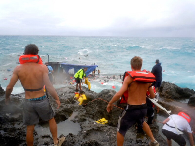 Reddingswerkers halen bootvluchtelingen uit het water aan de rotskust van het Australische Christmas Island.