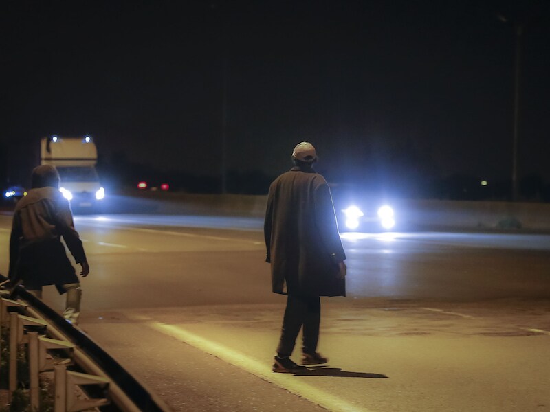 Migranten steken de snelweg met voorbijrazend verkeer over, op weg naar de ingang van de Eurotunnel.