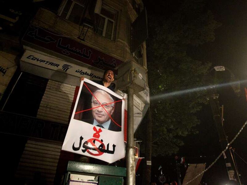 Een betoger toont een foto van Shafiq met een rood kruis over.