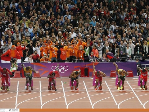 De start van de 100m-finale. Achter de lopers ligt een fles, de Nederlandse delegatie, met daarbij Edith Bosch, staat in de buurt.