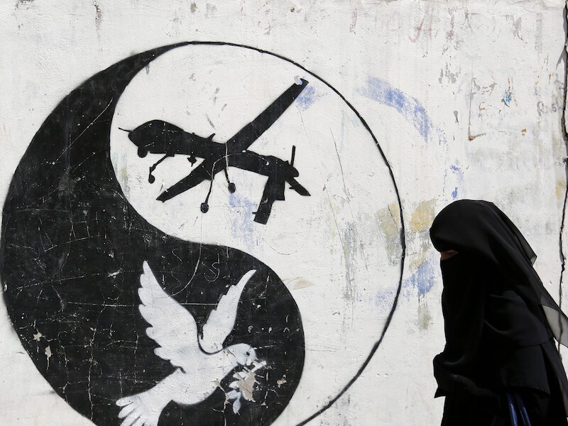 Een Jemenitische vrouw wandelt voorbij graffiti waarin de Amerikaanse droneaanvallen op Jemen worden aangeklaagd.