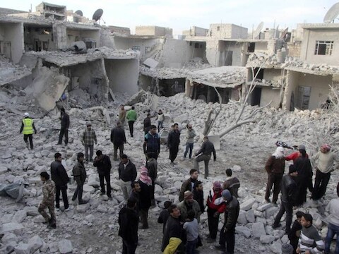 Mensen lopen tussen de brokstukken van vanuit de lucht gebombardeerde huizenblokken in Aleppo.