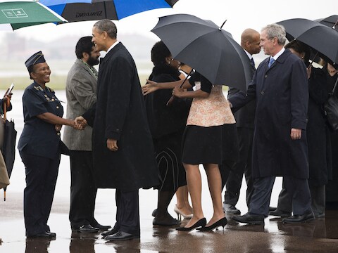 President Obama, Michelle Obama (onder paraplu) en George W. Bush bij aankomst op Waterkloof Air Base vliegveld in Zuid-Afrika.
