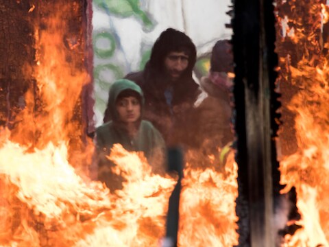 Migranten kijken hoe houten hutjes afbranden in de Jungle van Calais.