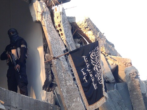 Een strijder van al-Nusra naast de vlag van de groepering in een ingestort gebouw, net als IS getroffen door Amerikaanse luchtaanvallen.