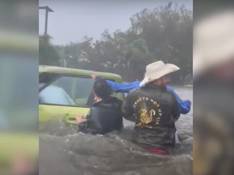Op de beelden is te zien hoe een groep mannen – die tot hun middel in het water staan – de oudere man van zijn ondergelopen auto wegdragen. 