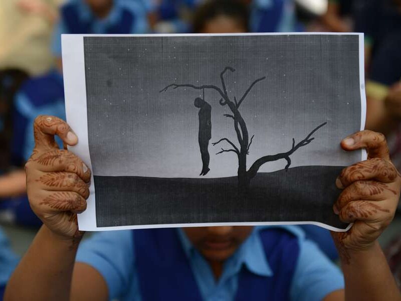 Een schoolmeisje houdt een papier met een man hangend aan een boom op tijdens een protest tegen verkrachtingen in haar land.