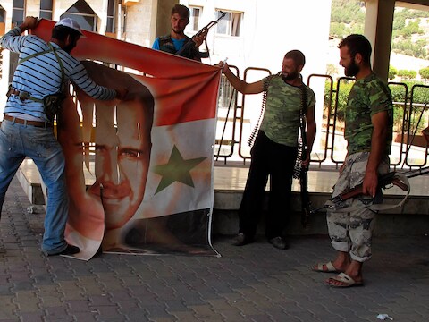 Syrische rebellen vernielen een banner van de president Bashar al-Assad.
