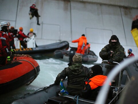 Een lid van de Russische kustwacht richt een geweer op een lid van Greenpeace.
