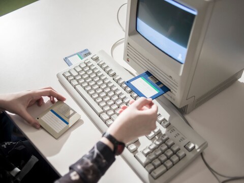 Een beeld dat zo uit eind jaren 80, begin jaren 90 zou kunnen komen. Een computergebruiker - in dit geval een Macintosh - heeft twee diskettes bij de hand om gegevens op te slaan of uit te lezen.