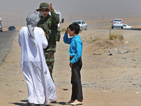 Een Koerdische soldaat helpt een Irakese man bij een controlepost tussen Mosul en Irbil.