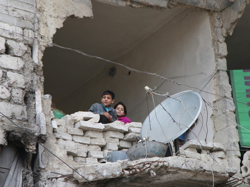 Kinderen kijken naar buiten in een huis dat zwaar geleden heeft onder het oorlogsgeschut in Aleppo.