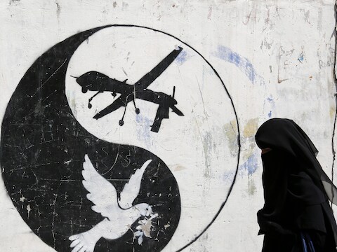 Een Jemenitische vrouw wandelt voorbij graffiti waarin de Amerikaanse droneaanvallen op Jemen worden aangeklaagd.