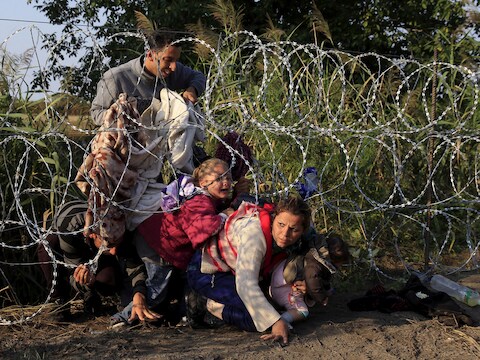Syrische migranten kruipen onder een hek aan de Hongaars-Servische grens.