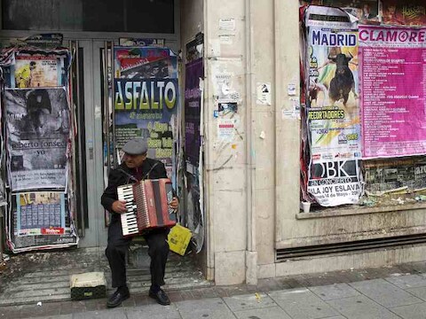 Op de drempel van een gesloten bankfilliaal speelt een Spaanse man op zijn accordeon.