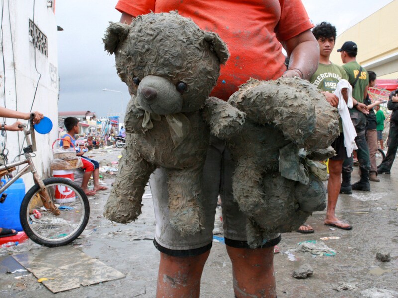 Een vrouw draagt de knuffels van haar dochter in het zwaar getroffen Tacloban.
