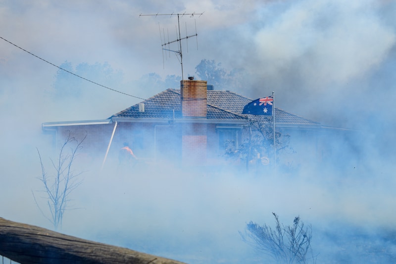 Una bandera australiana ondea mientras los bomberos rocían una casa en Longwood.