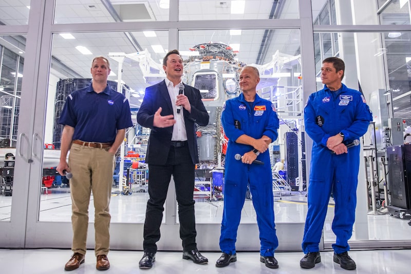 Elon Musk, eigenaar van SpaceX en de twee astronauten aan zijn linkerzijde (rechts in beeld).