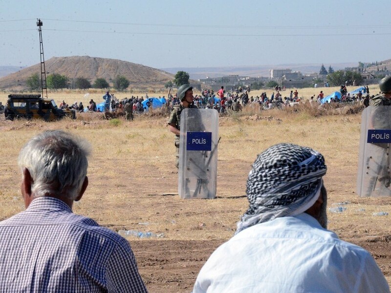 Turkse grenswachters en Syrische vluchtelingen die de grens willen oversteken.