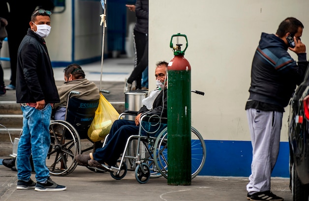 Mensen wachten op hulp bij een ziekenhuis in Lima. Een man in een rolstoel krijgt zuurstof via een grote fles die naast hem staat.