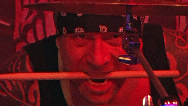 Phil Baheux bergt zijn drumstok even op terwijl hij de hoogte van een cymbaal aanpast.