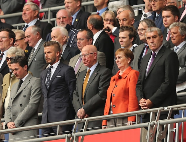 In de tribunes van l naar r: David Beckham, Sir Bobby Charlton en gewezen doelman Peter Shilton
