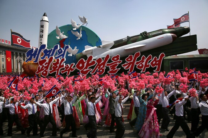 Noord-Koreanen zwaaien met de vlag van het land en plastic bloemen terwijl een vloot met raketten en het opschrift 'Voor vrede en stabiliteit in de wereld' voorbijkomt tijdens de militaire parade ter ere van de 'Dag van de Zon'.