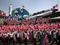 Noord-Koreanen zwaaien met de vlag van het land en plastic bloemen terwijl een vloot met raketten en het opschrift 'Voor vrede en stabiliteit in de wereld' voorbijkomt tijdens de militaire parade ter ere van de 'Dag van de Zon'.
