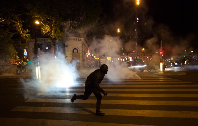 Een demonstrant rent weg in Parijs nadat de politie wolken traangas verspreid. In de Franse hoofdstad zijn na de uitslag van de eerste ronde van de presidentsverkiezingen mensen de straat opgegaan.