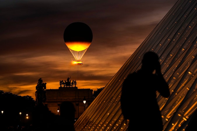 Een man maakt een foto van de piramide bij het Louvre met op de achtergrond de olympische vlam die opstijgt vanuit de Tuilerieën.