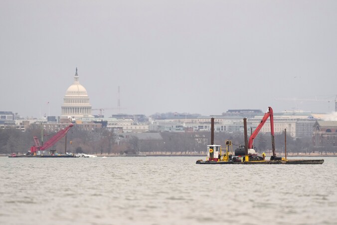Bergingsteams zijn aan het werk op de Potomac-rivier, terwijl op de achtergrond het Capitool in Washington zichtbaar is.