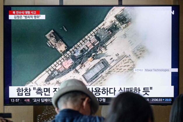 Mensen kijken in Zuid-Korea naar een nieuwsitem over de mislukte lancering van het oorlogsschip in Noord-Korea. In beeld een satellietfoto van de torpedojager nog intact op de kade.