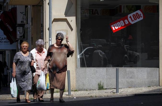 Drie oude vrouwen lopen langs een gesloten winkel in de Portugese hoofdstad Lissabon met sticker "alles aan 1 euro".