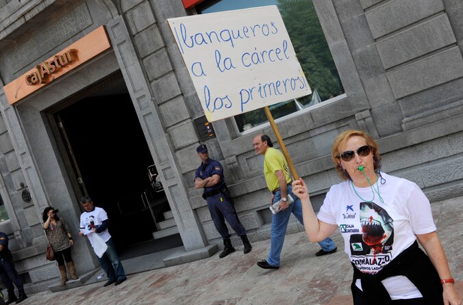 Aan het hoofdkwartier van de Liberbank in Oviedo werd vandaag geprotesteerd. Een ontevreden vrouw houdt een bord omhoog waarop staat: "Bankiers als eerste naar de gevangenis!"