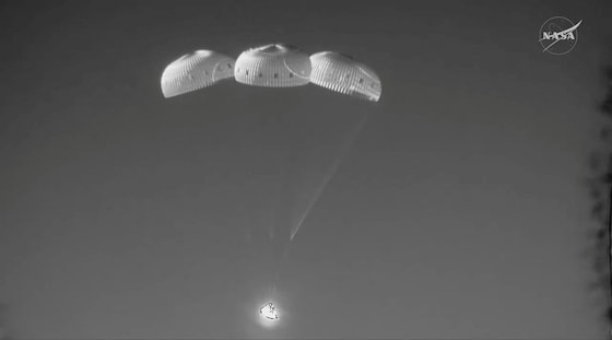 De drie hoofdparachutes klappen open terwijl de capsule naar beneden vliegt.