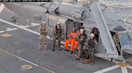 Crewleden Christina Koch en Victor Glover zwaaien naar de camera vanuit de helikopter die hen naar het marineschip bracht.