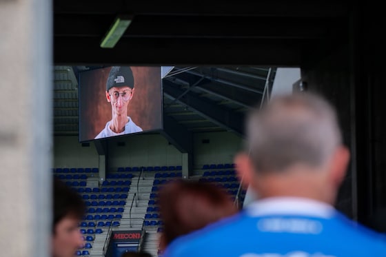 De deuren van de Cegeka Arena zijn geopend en bezoekers mogen plaatsnemen op de tribune. Op het grote scherm wordt een foto van Michiel getoond.