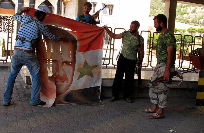 Syrische rebellen vernielen een banner van de president Bashar al-Assad.