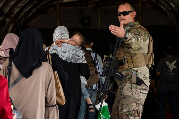 Een Amerikaanse soldaat leidt vrouwen en kinderen een evacuatievliegtuig in op de luchthaven van Kaboel.