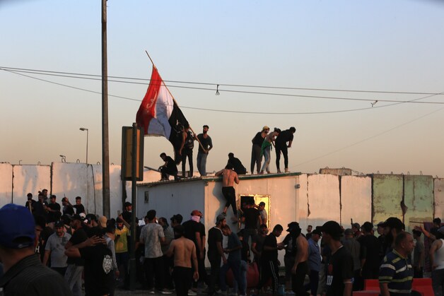 epa10145842 Supporters of Iraqi Shiite cleric Muqtada al-Sadr, head of the Sadrist movement, wave the national flag during clashes with anti-riot forces near the office of prime minister, Baghdad, Iraq, 29 August 2022. The leader of the Sadrist movement Muqtada al-Sadr announced on 29 August his final retirement and the closure of institutions, prompting supporters, who had been on a sit-in at the Iraqi parliament since July, to storm the Republican Palace, that houses the office of the prime minister, while a curfew was announced in Baghdad from 3:30pm (12:30 GMT).  EPA/AHMED JALIL